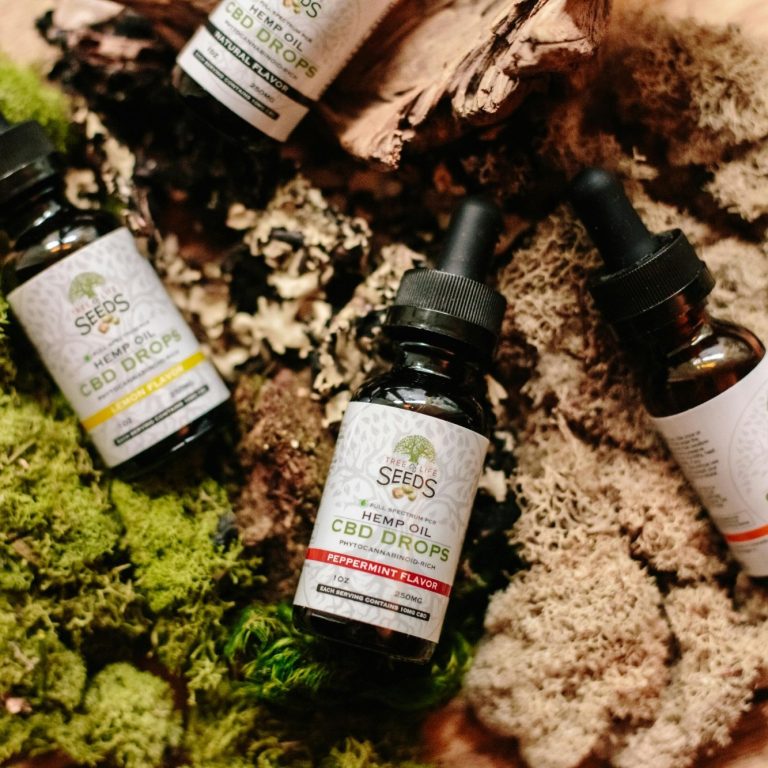 Quatre flacons d'huiles essentielles au CBD sur un fond de mousse et d'écorce.